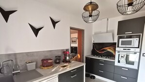 Eine moderne Küche mit Geschirrspüler, Mikrowelle, Backofen und Spüle. Es sind dekorative Wandbilder und ein außergewöhnliches Lichtelement vorhanden.