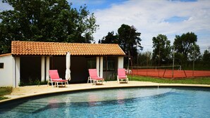 A swimming pool with two pink lounge chairs and a covered seating area with a tiled roof. - Charming Mas for rent by the week  (Arles)
