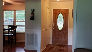 A hallway with a wooden door, a dining area with a table and chairs, and a window with blinds. - Beaufort Family Home (Beaufort)