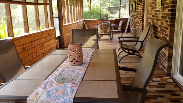 A covered patio area with wooden walls, a tiled floor, and a table set with a patterned tablecloth, chairs, and a decorative vase. - Beaufort Family Home (Beaufort)