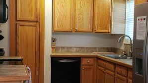 A kitchen with wooden cabinets, a dishwasher, a refrigerator, and a patterned rug. - Beaufort Family Home (Beaufort)