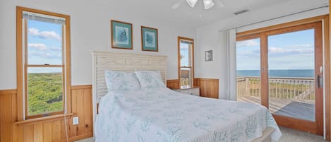 A bedroom with a bed, a ceiling fan, and a view of the ocean through a sliding glass door.