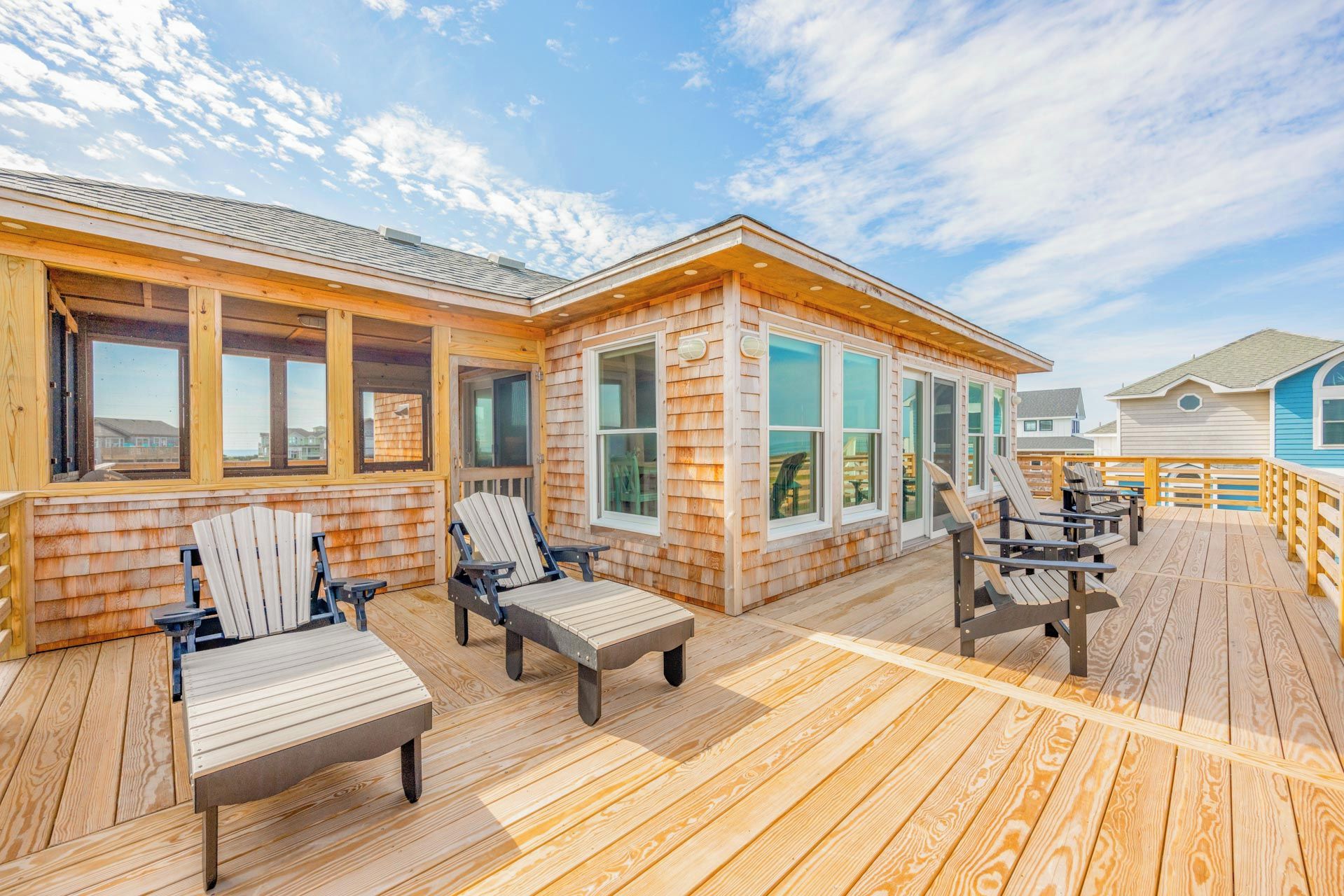Une terrasse en bois avec des sièges extérieurs et une pièce fermée par des baies vitrées.