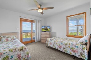 A bedroom with two beds, a ceiling fan, a television, and a window with a view of the sea. - Soundfront Home w/ Hot Tub, Easy Windsports Access, Sound Boardwalk, and More! (Frisco)