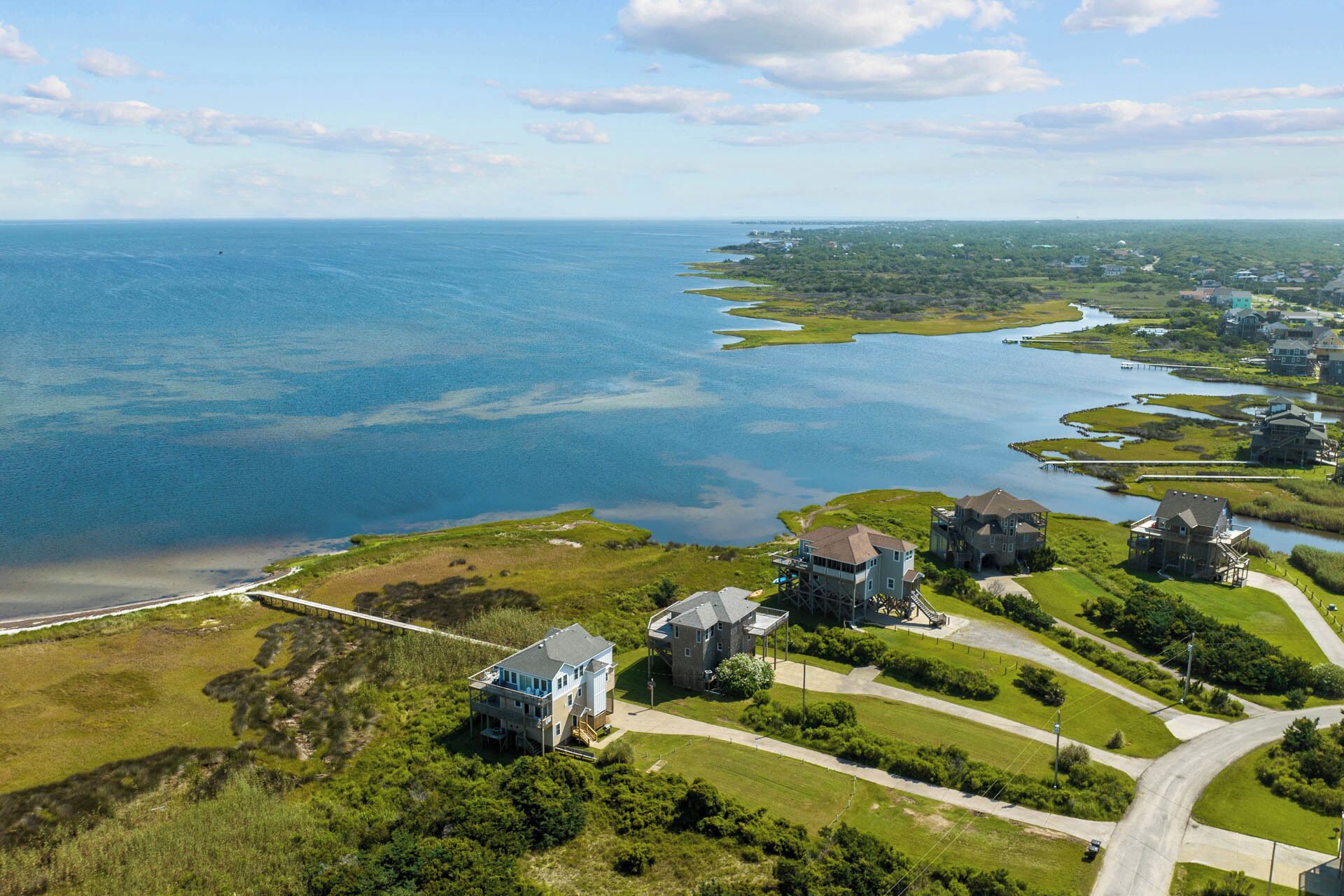 Vue aérienne d’une zone résidentielle côtière, avec des maisons, une plage et une vaste étendue d’eau.