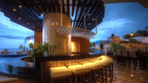 Zona de bar con una barra curva, taburetes acolchados y una lámpara colgante.