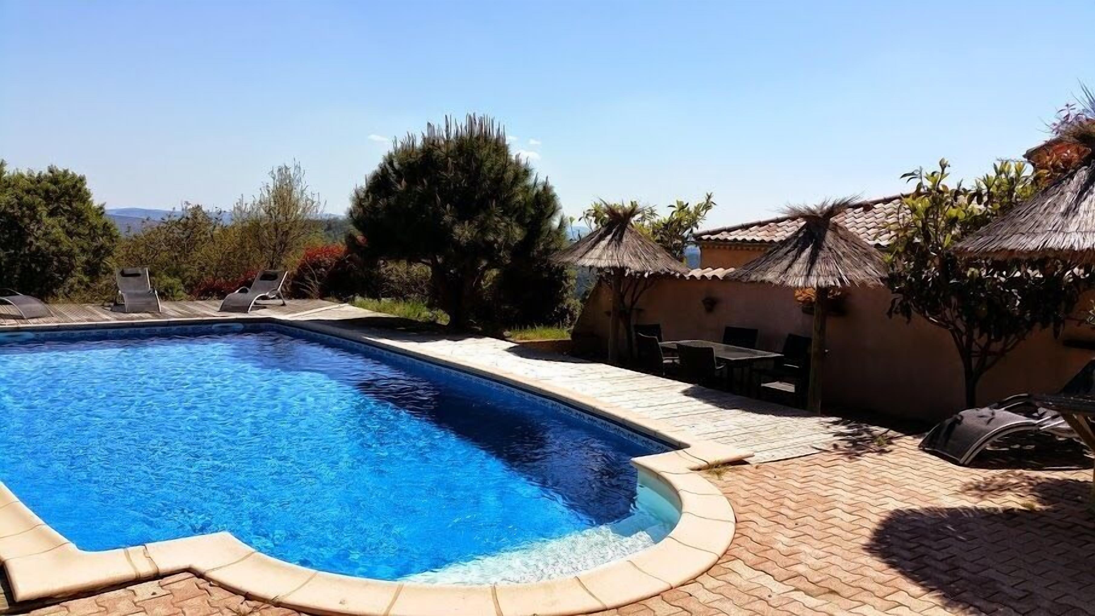 A rectangular swimming pool with a tiled deck, surrounded by lounge chairs and a small table.