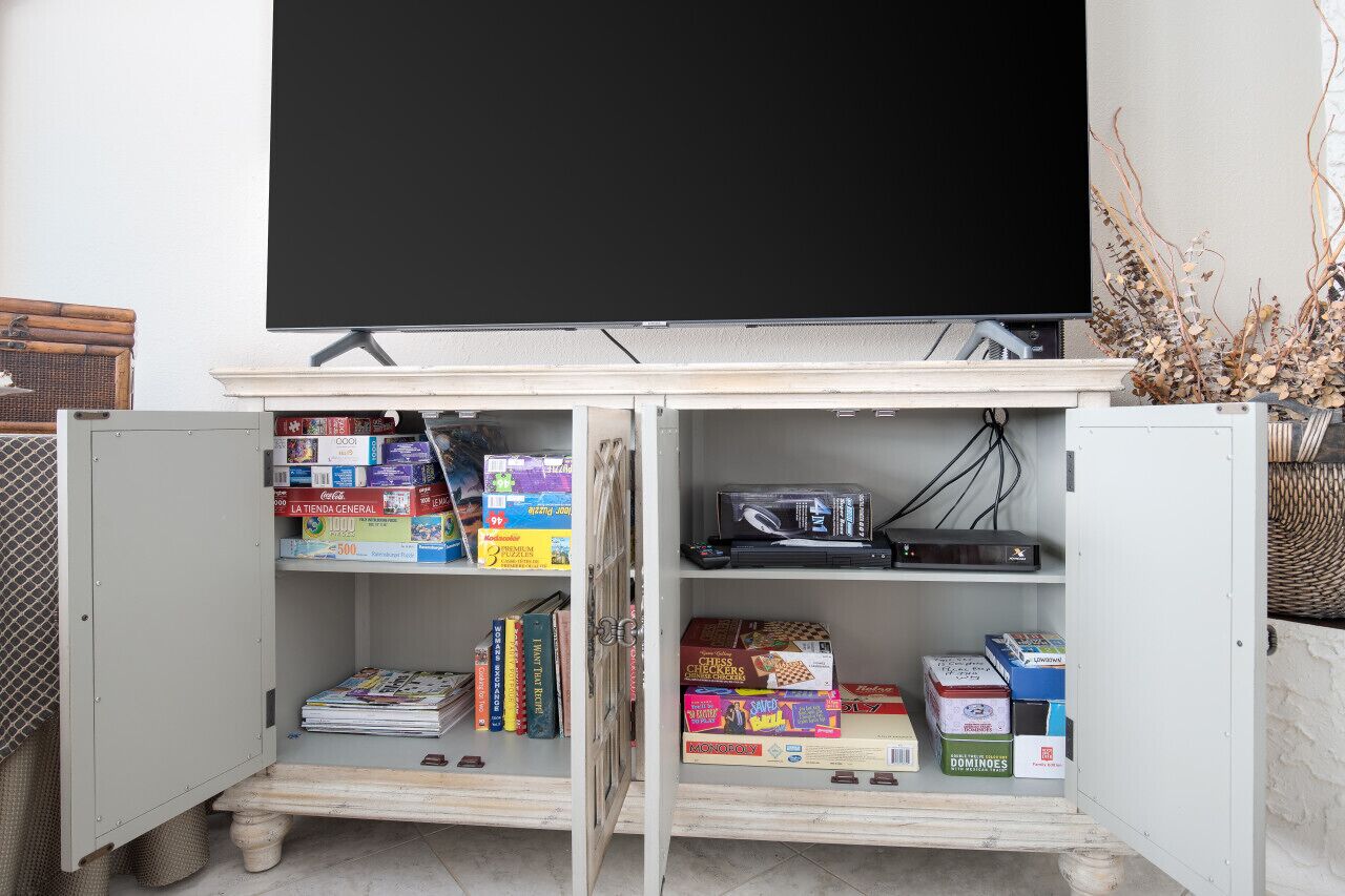 A room with a television mounted on a cabinet, shelves with books and board games, and a wicker basket on the right.