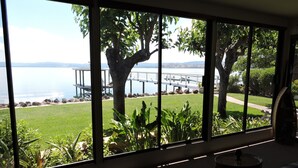 A room with large windows offering a view of a lake, a dock, and a grassy area with trees.