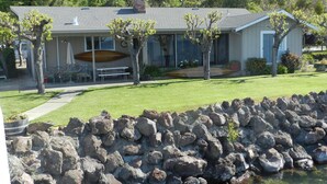 A house with a stone retaining wall, a lawn, and a patio area with outdoor furniture.