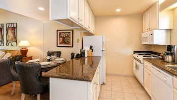 A modern kitchen with white cabinets, a granite countertop, and a dining area with a table set for two.