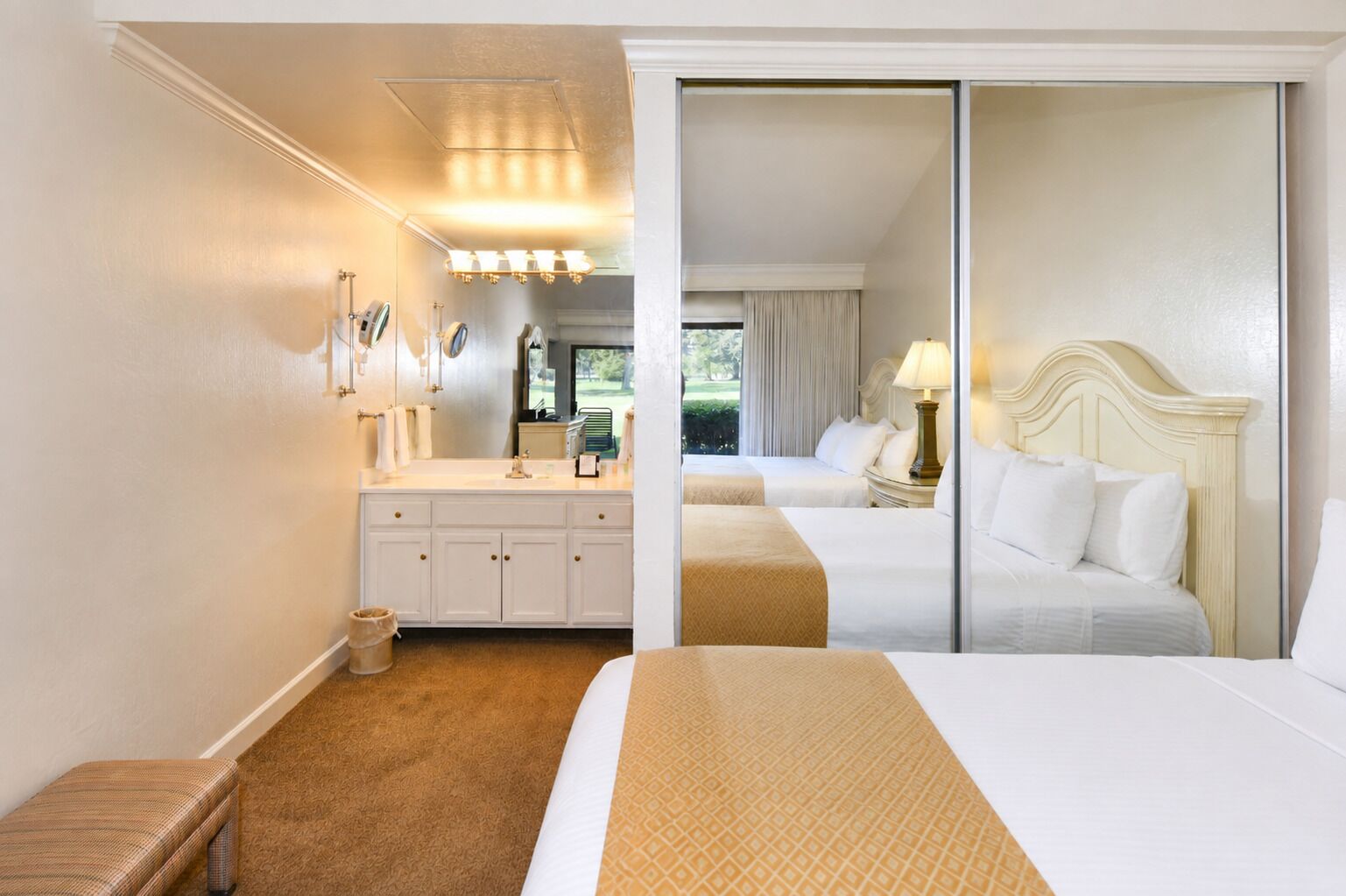 Habitación de hotel con una cama grande, una cama adicional, baño con tocador y vistas al exterior.