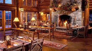 Un interior acogedor y rústico con muebles de madera, chimenea de piedra y vistas al exterior.