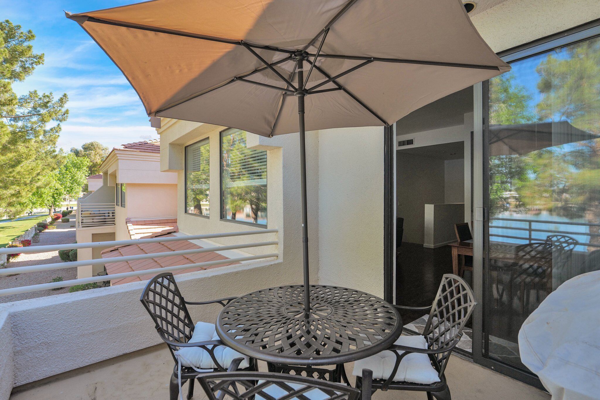Une terrasse extérieure avec une table ronde et des chaises, un grand parasol et une vue sur une piscine, visible à travers une porte vitrée.