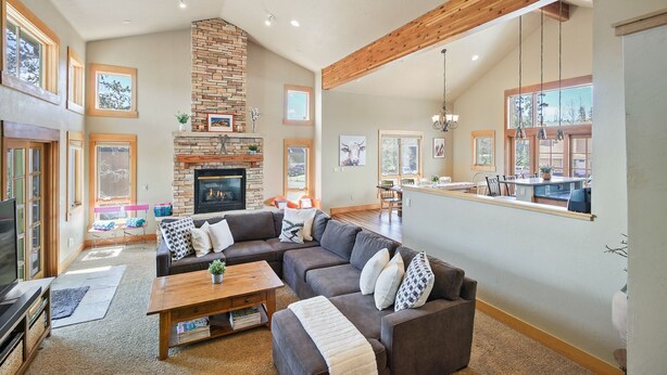 A spacious living room with a stone fireplace, a large sofa, and a dining area with a kitchen counter. - Hot Tub. Awesome Views. Close to ski areas. Garage. Fully Stocked Kitchen. (Silverthorne)