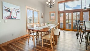 A dining area with a wooden table and chairs, large windows, and a chandelier. - Hot Tub. Awesome Views. Close to ski areas. Garage. Fully Stocked Kitchen. (Silverthorne)