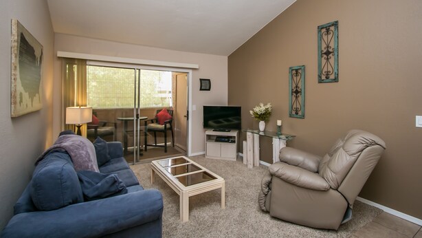 A living room with a blue sofa, a glass coffee table, a recliner, a TV, and a sliding glass door leading to a balcony. - GREAT condo rental conveniently located in Mesa/Phoenix   (Mesa)