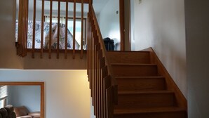 Een houten trap met uitzicht op een kamer met een kamerbreed gordijn en een bruine leren fauteuil.