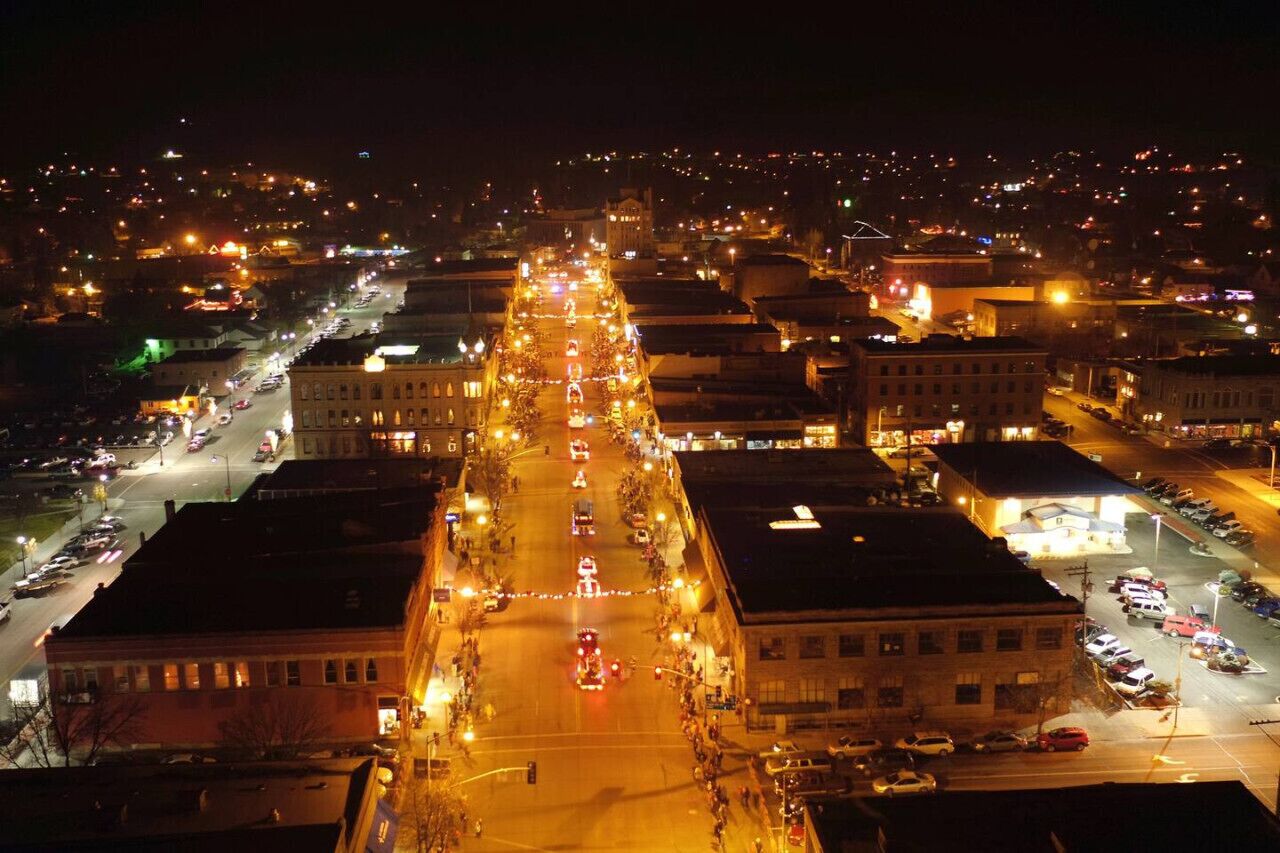 A nighttime aerial view of a city street lined with buildings, illuminated by streetlights and vehicle headlights.