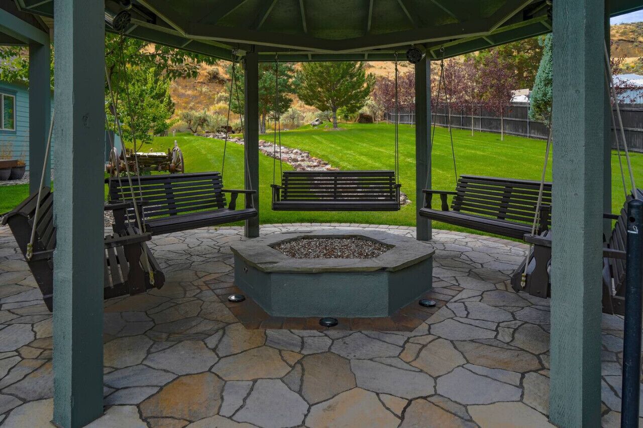 A gazebo with stone flooring, two benches, and a fire pit.