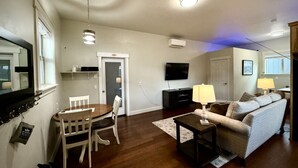 A living room with a dining table, chairs, a sofa, a TV, and a lamp. - Claim Jumpers Cottage (Baker City)