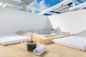 A modern spa area with a hot tub, two white cushioned seating areas, and a champagne bottle. - Luxury Ocean View Penthouse w/ Private Rooftop Hot Tub, Steps to Beach (Miami Beach)