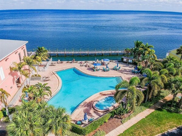 A resort with a large pool, palm trees, and a pier extending into the water.