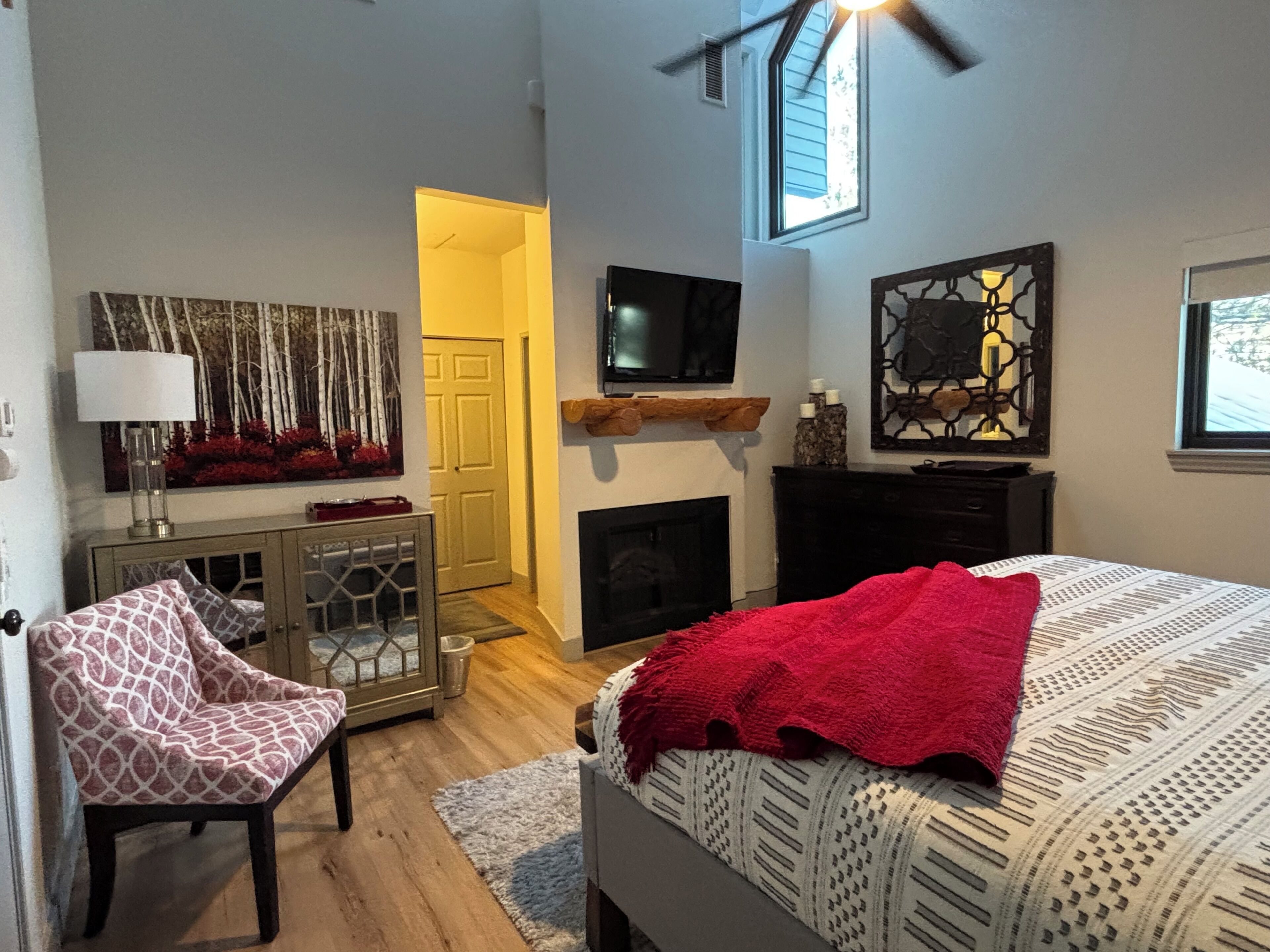 Une chambre à coucher comprenant un lit, une télévision, une cheminée, un fauteuil et une porte donnant sur une autre pièce.