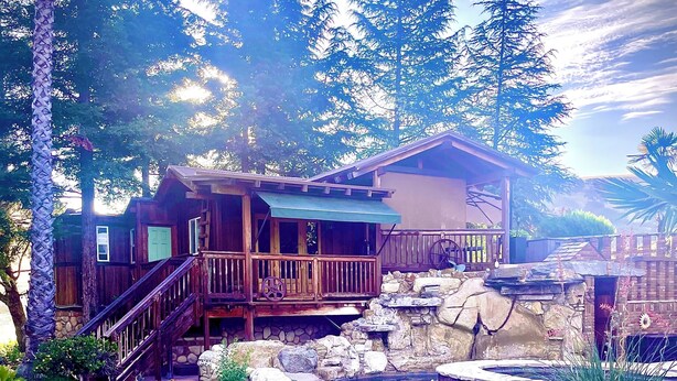 A wooden cabin with a deck, a stone wall, and a clear blue pool surrounded by rocks and trees. - TREE CABIN FOR 2🌲Unique cabin close to San Luis Obispo, Morro Bay & Paso Robles (Templeton)