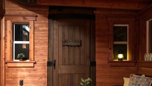 A wooden cabin with a large door, a wicker chair, a small table with a plant, and a window with a lantern. - TREE CABIN FOR 2🌲Unique cabin close to San Luis Obispo, Morro Bay & Paso Robles (Templeton)