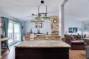 A modern kitchen with a marble countertop, a hanging light fixture, and a wooden accent wall. - Cherry Lane Sanctuary, Rustic Retreat on 6 Acres with Sauna/ Hot Tub/ Pool/ Golf (Henryville)
