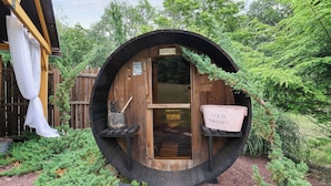 Een houten, vatvormig gebouw met een bord voor koude dranken, omringd door groen.