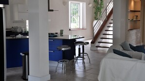 Een moderne keuken met een centraal eiland, een zithoek met een bank en een trap naar een hoger gelegen verdieping.