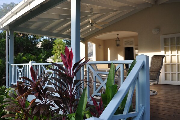 A covered outdoor area with a wooden deck, white railings, and a ceiling fan.