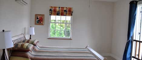 Ein Schlafzimmer mit Bett, Deckenventilator, Fenster mit Blick ins Grüne und einer Wand-Klimaanlage.