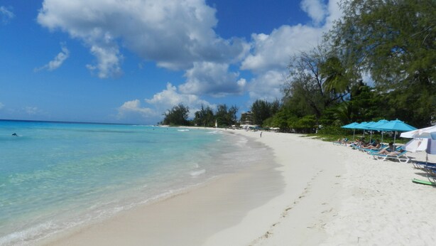 Een strand met helder turquoise water, wit zand en een rij blauwe parasols.