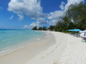 A beach with clear turquoise water, white sand, and a row of blue umbrellas.