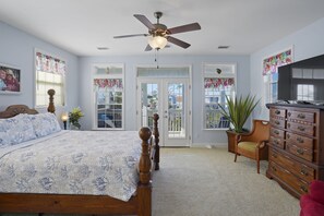 A bedroom with a bed, dresser, TV, and a ceiling fan.
