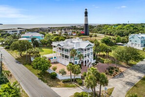 Stunning views of a lighthouse from this two-story home's balcony, surrounded by lush greenery and palm trees.
