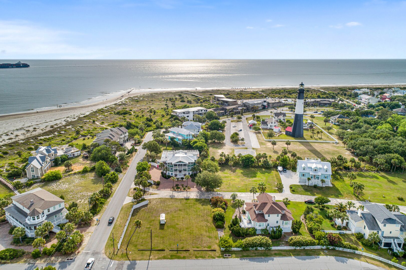 An aerial view of a coastal residential area with houses, a lighthouse, and a beach.
