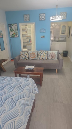 A living room with a sofa, a coffee table, and a bed with a patterned bedspread. - Secluded Studio@Sky Castles, Ocho Rios - cozy, modern, secluded w/ ocean views (Ocho Rios)