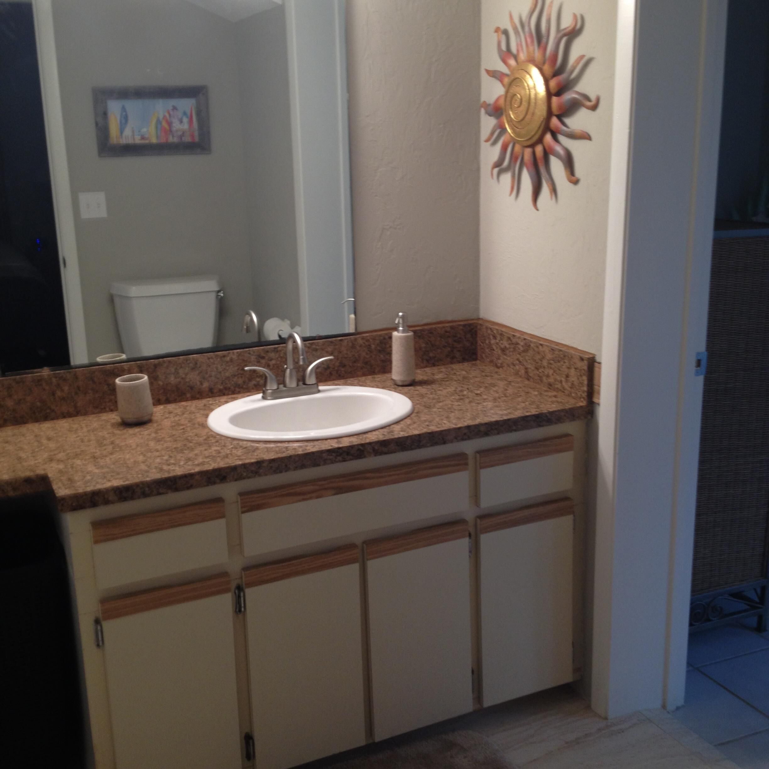 A bathroom with a white sink, a mirror, and a decorative sun on the wall.