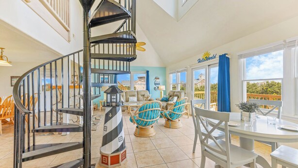 A spacious room with a spiral staircase, wicker chairs, a dining table, and large windows offering a view of the outside.