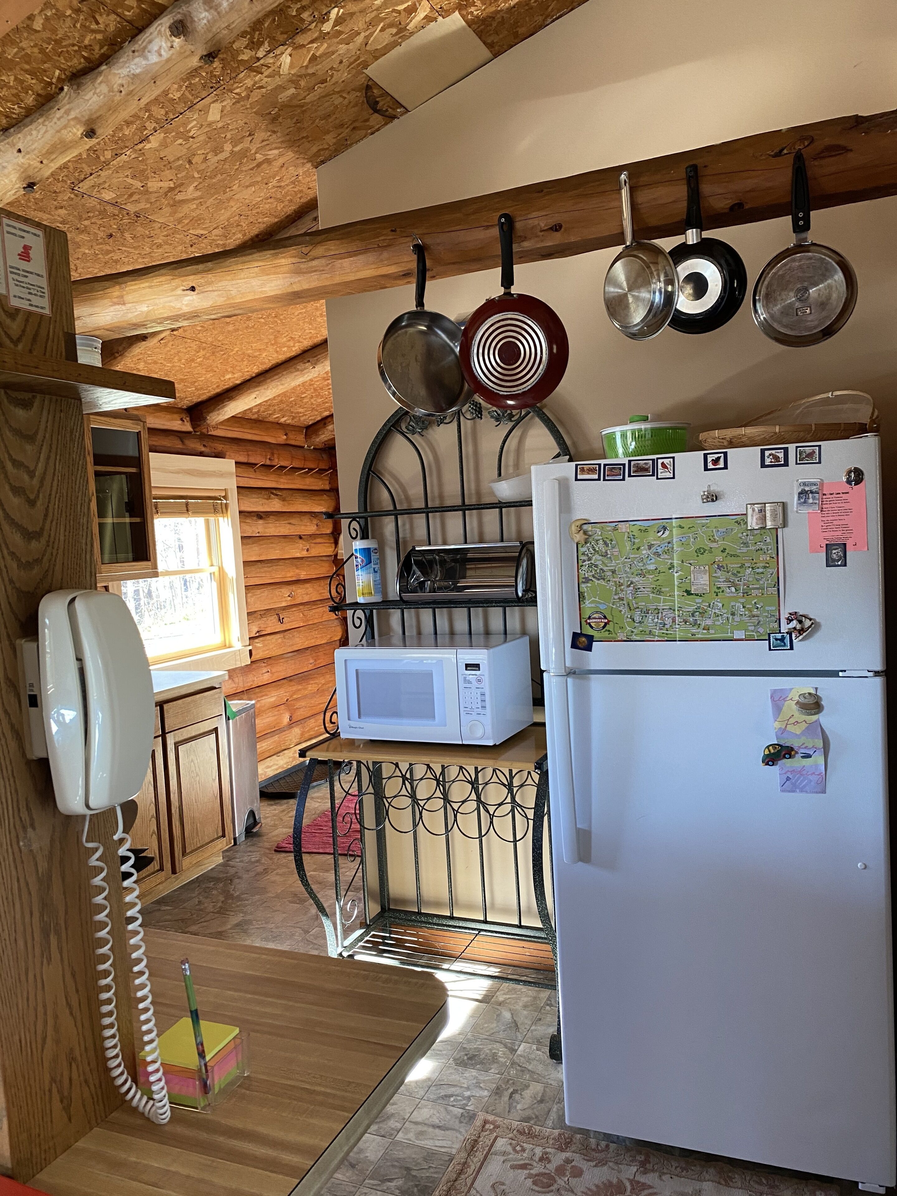 A compact kitchen with a wooden ceiling, a white refrigerator, a microwave, and a stove.