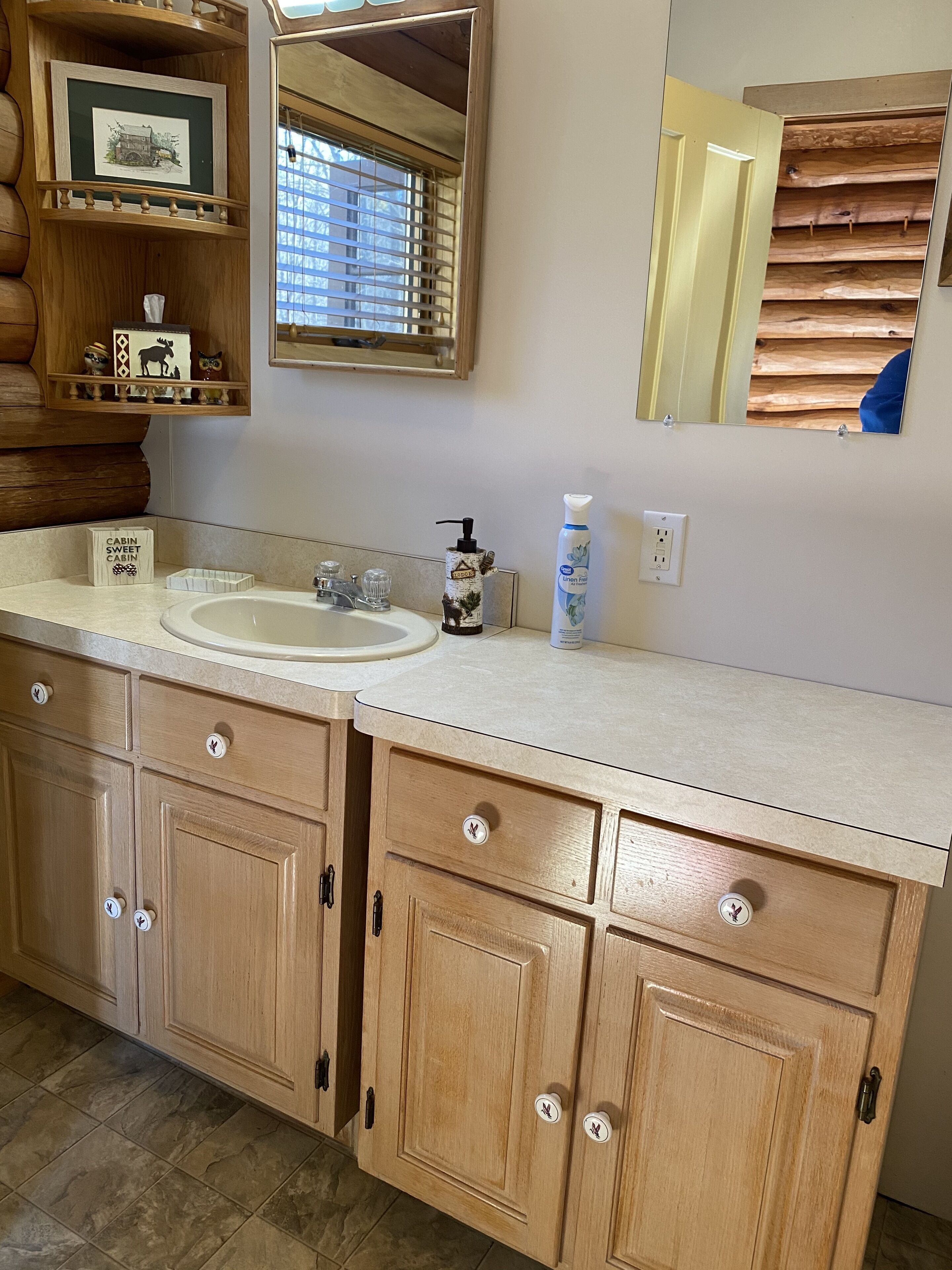 A wooden cabin-style bathroom with a large sink, wooden cabinets, a mirror, and a window with blinds.