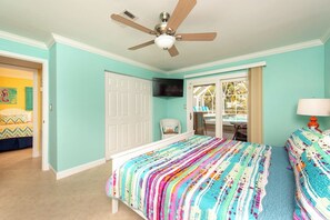 Ein Schlafzimmer mit Bett, Deckenventilator, Fernseher und Blick auf einen Pool durch eine Glastür.