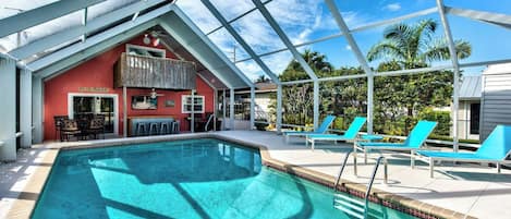 A pool area with a covered section, lounge chairs, and a bar area with a red wall and a sign that reads "POOL RULES".