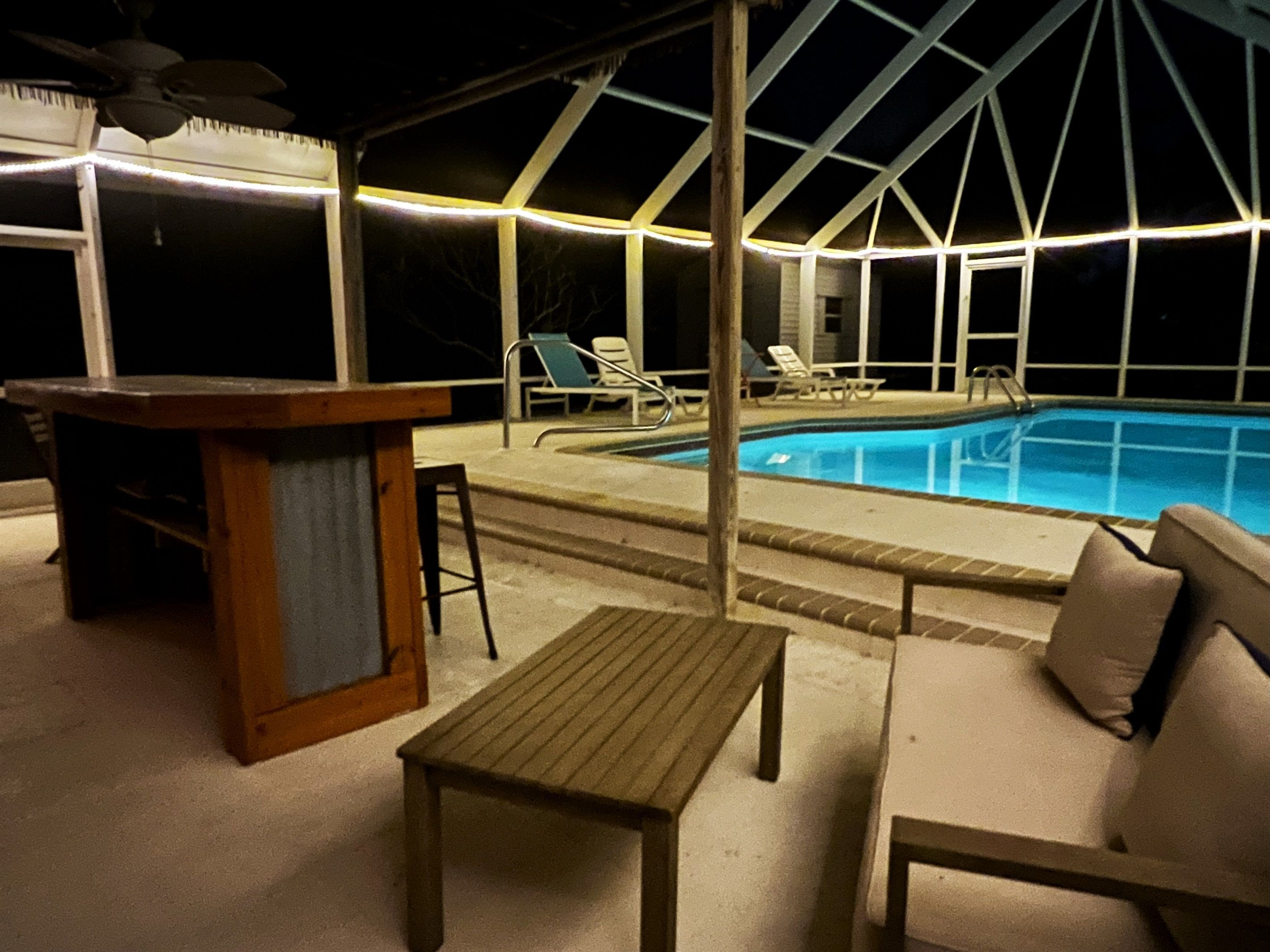An outdoor pool area with a covered seating area, a wooden table, and lounge chairs.