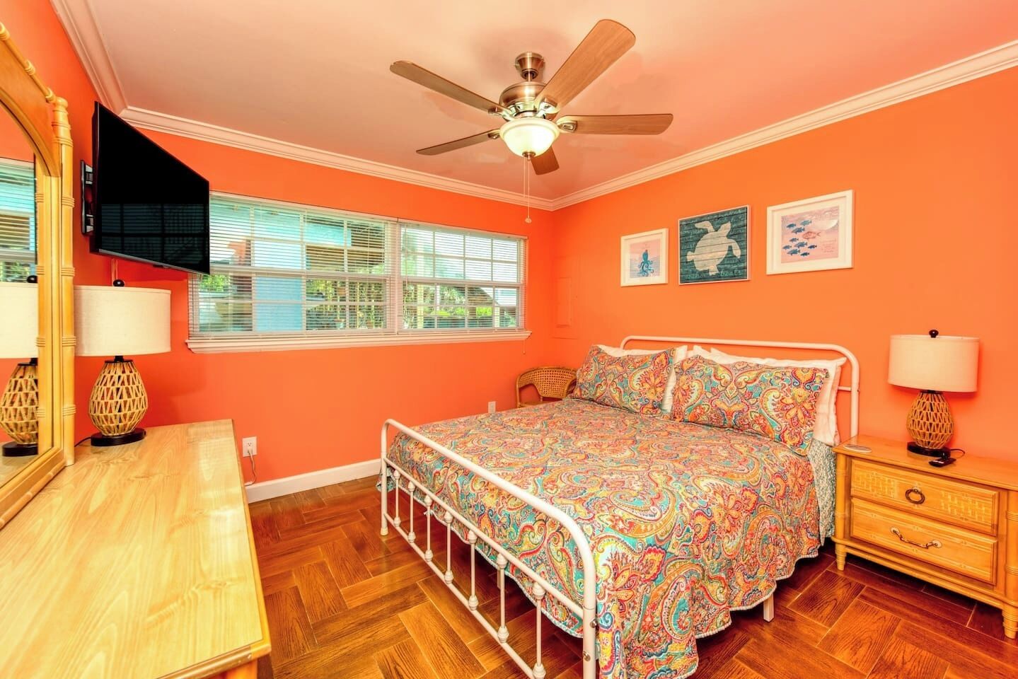 Quarto com cama, ventoinha no teto, janela com persianas, mesa de cabeceira com abajur e cômoda.