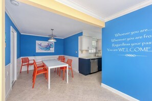 Ein Essbereich mit einem weißen Tisch und orangefarbenen Stühlen, einer blauen Akzentwand und einer Küche mit weißen Schränken.